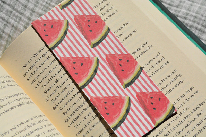 Handcrafted linen bookmark with a watercolor watermelon pattern resting inside an open book, perfect for summer reading.
