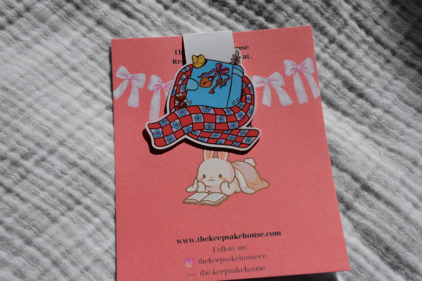 Handmade magnetic bookmark featuring a book wrapped in a cozy scarf design on a pink Keepsake House backing card
