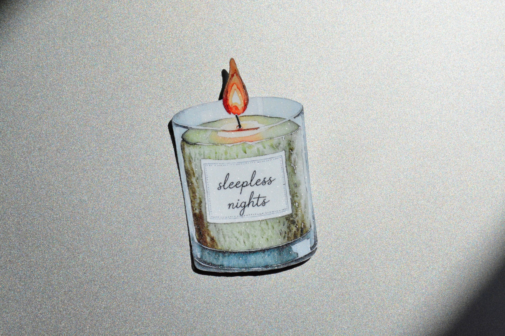 Sleepless Nights holographic watercolor candle sticker on a gold glittery surface