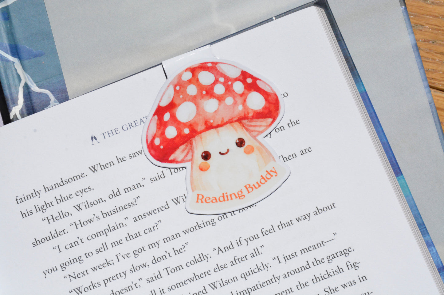 Reading Buddy mushroom magnetic bookmark resting on an open book, featuring a cute watercolor red mushroom design for book lovers.