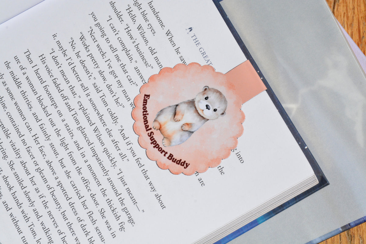 Cute otter magnetic bookmark clipped inside an open book, featuring a watercolor "Emotional Support Buddy" design for book lovers and readers.