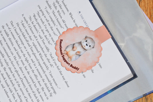 Cute otter magnetic bookmark clipped inside an open book, featuring a watercolor "Emotional Support Buddy" design for book lovers and readers.