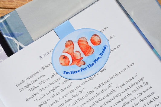 Cute clownfish magnetic bookmark clipped inside an open book, featuring the phrase "I'm Here For The Plot, Buddy" for book lovers and readers.