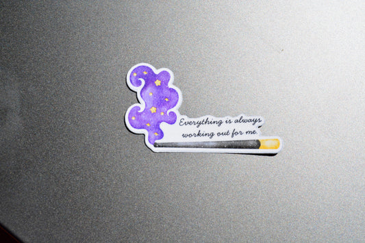 A die-cut sticker featuring a purple cloud with yellow stars and the quote 'Everything is always working out for me' next to a progress bar, shown on a textured gray surface.