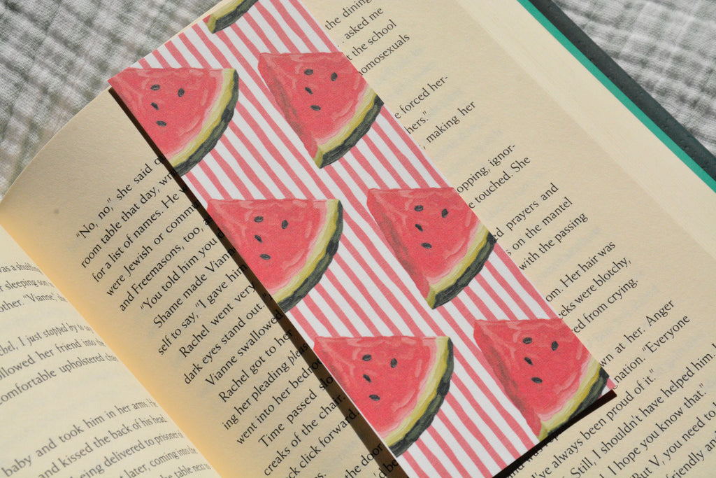 Handcrafted linen bookmark with a watercolor watermelon pattern resting inside an open book, perfect for summer reading.