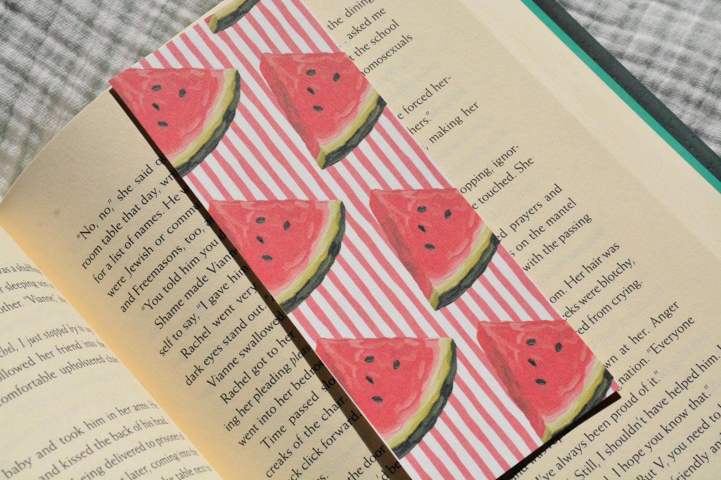 Handcrafted linen bookmark with a watercolor watermelon pattern resting inside an open book, perfect for summer reading.
