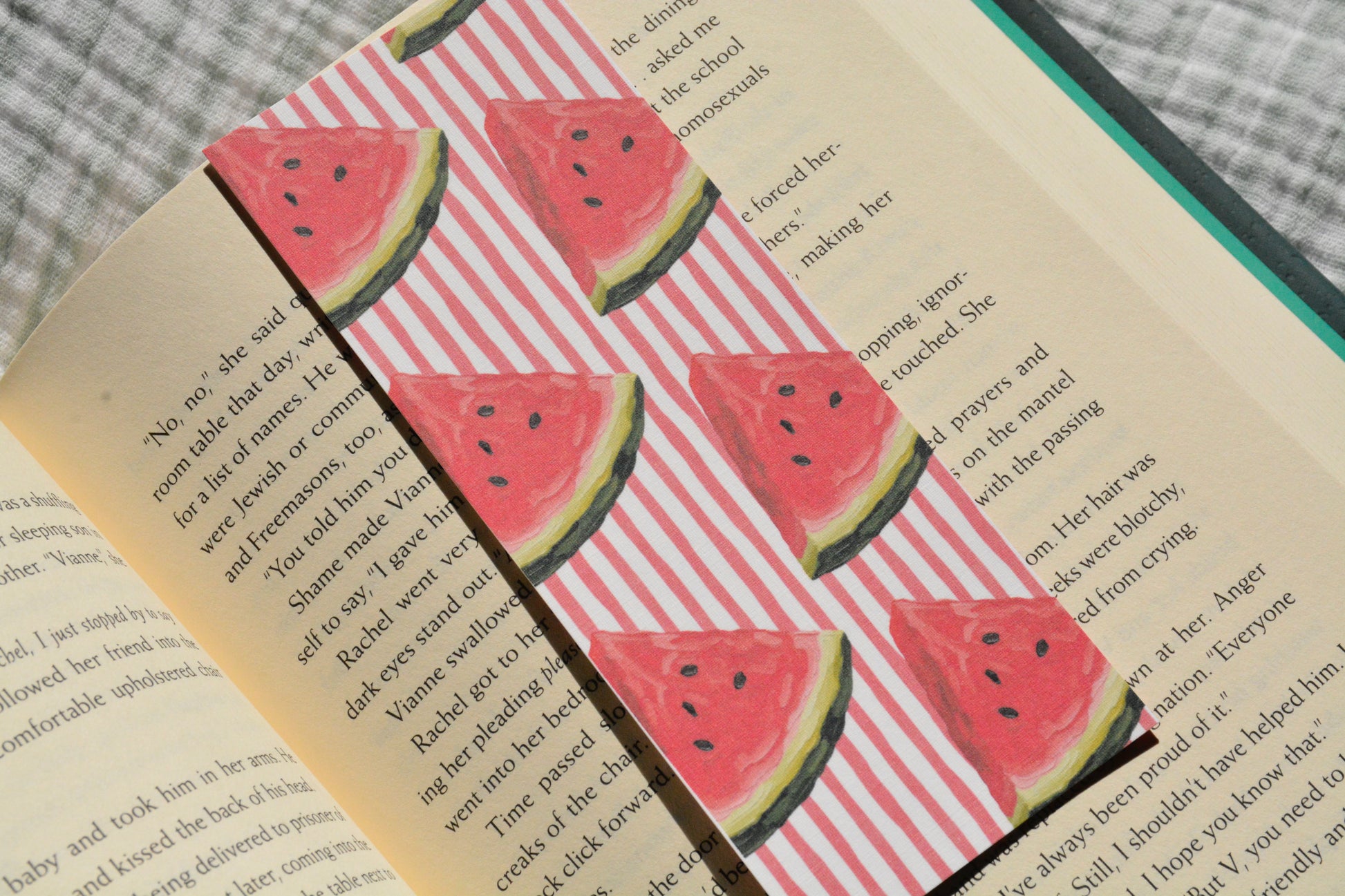 Handcrafted linen bookmark with a watercolor watermelon pattern resting inside an open book, perfect for summer reading.