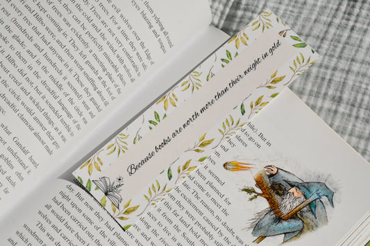 Double-sided linen bookmark with square corners displaying a botanical border and inspirational reading quote resting between book pages.