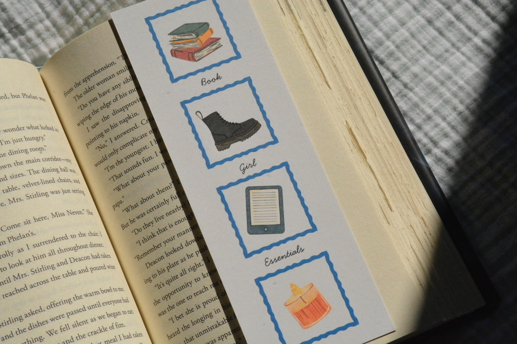 Book Girl Essentials linen bookmark with illustrations of books, a sweater, tote bag, library card, Kindle, boots, and a candle.