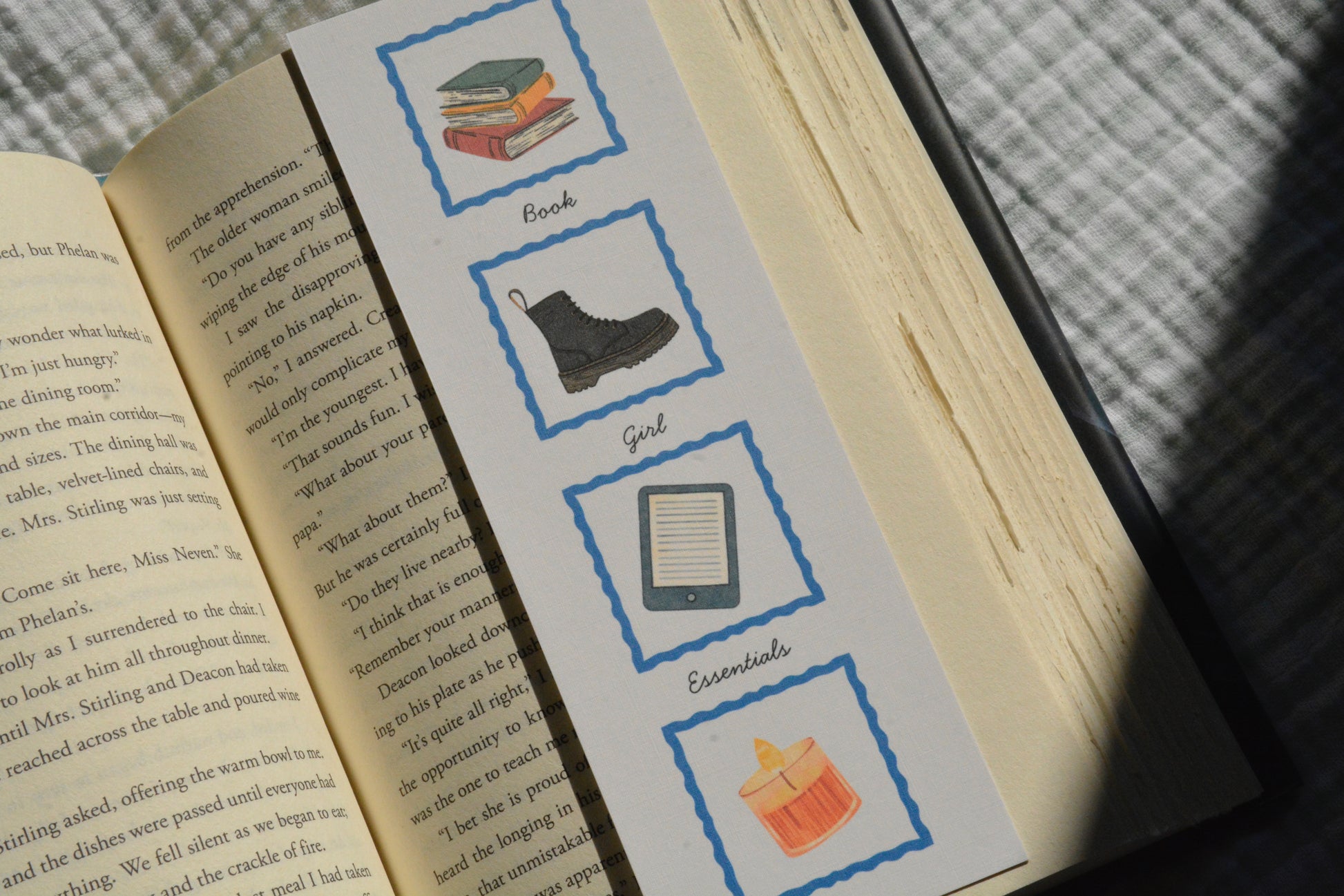 Book Girl Essentials linen bookmark with illustrations of books, a sweater, tote bag, library card, Kindle, boots, and a candle.