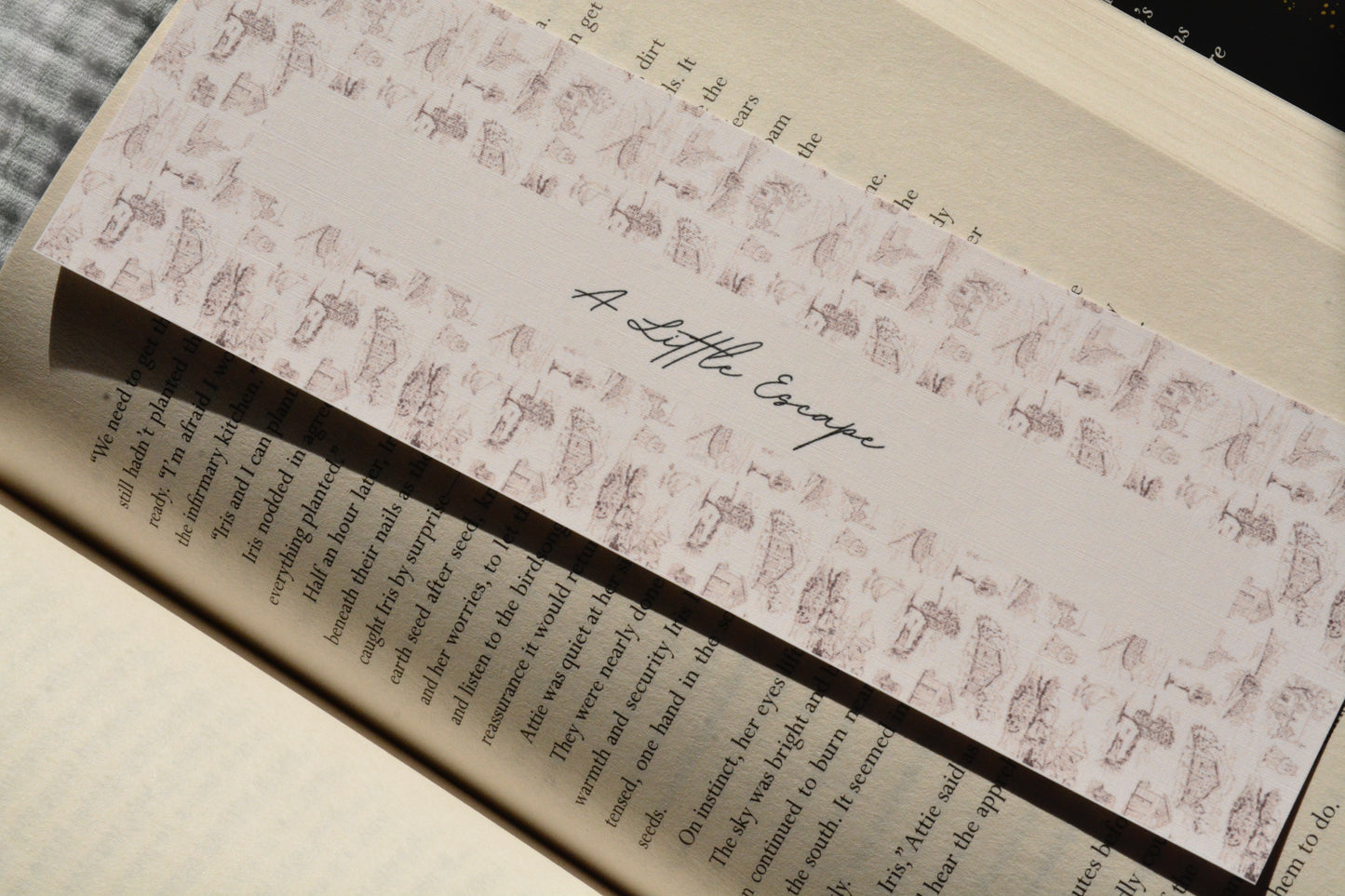 Elegant oversized linen bookmark with the quote "A Little Escape" resting between the pages of an open book.