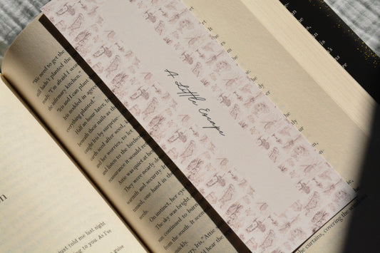 Oversized linen bookmark featuring a vintage toile-inspired pattern and the quote "A Little Escape" tucked inside an open book.