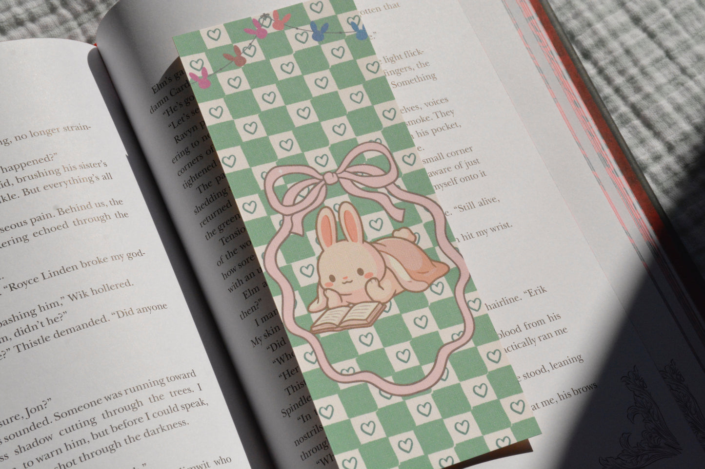 Cute linen bookmark featuring an adorable bunny reading a book on a pastel green checkerboard background tucked inside an open book.
