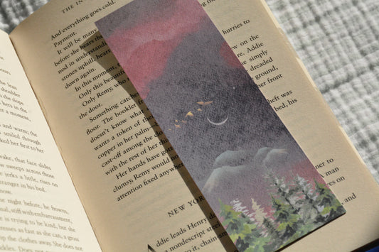 Double-sided linen bookmark featuring a dreamy moonlit forest on one side and a warm sunrise landscape with evergreen trees on the other.