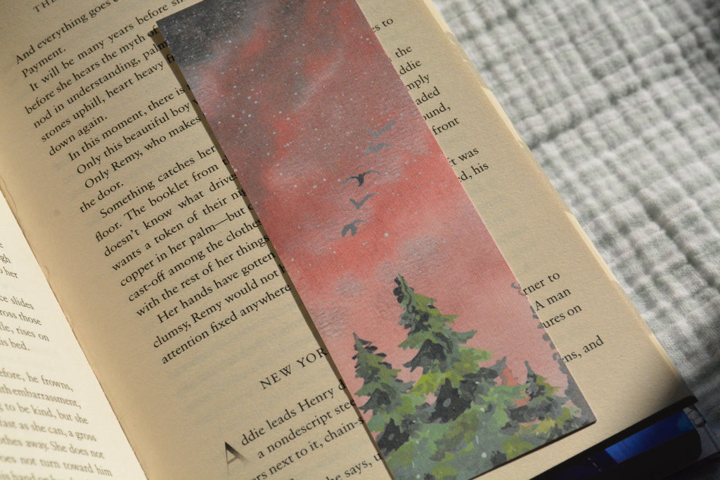 Handcrafted nature-inspired linen bookmark with peaceful day and night forest artwork tucked inside an open book.