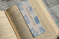 Linen bookmark featuring blue botanical leaves and the quote "Between the pages, I found peace" placed inside an open book.