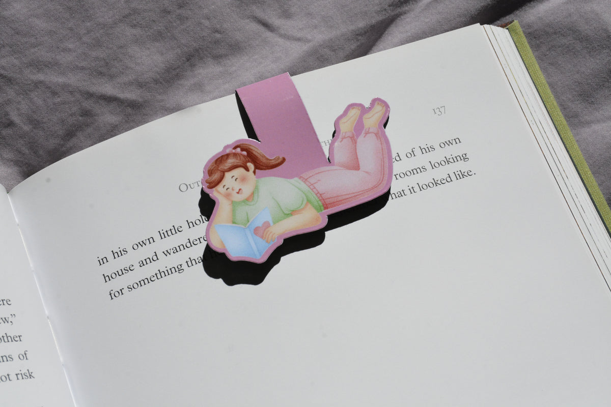 Little Escape magnetic bookmark featuring a girl reading, clipped securely inside an open book.