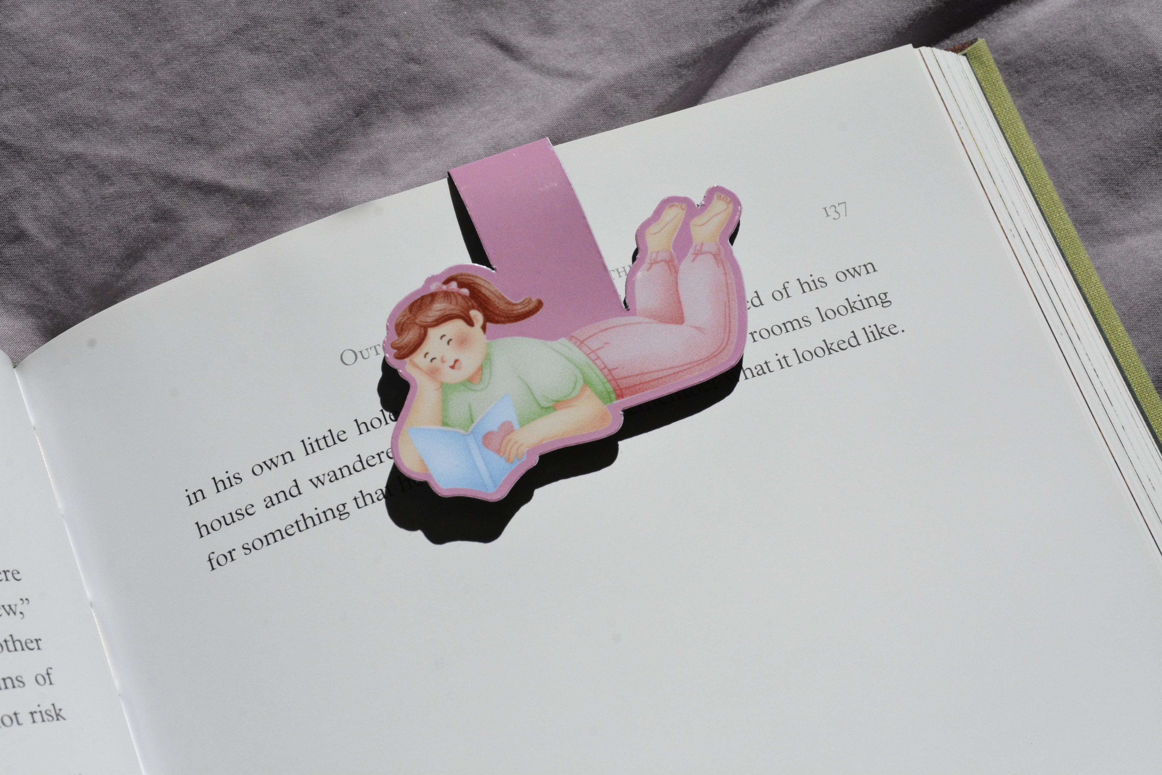 Little Escape magnetic bookmark featuring a girl reading, clipped securely inside an open book.
