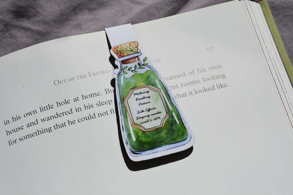 A magnetic bookmark shaped like a green potion bottle with illustrated text, placed on an open book page.