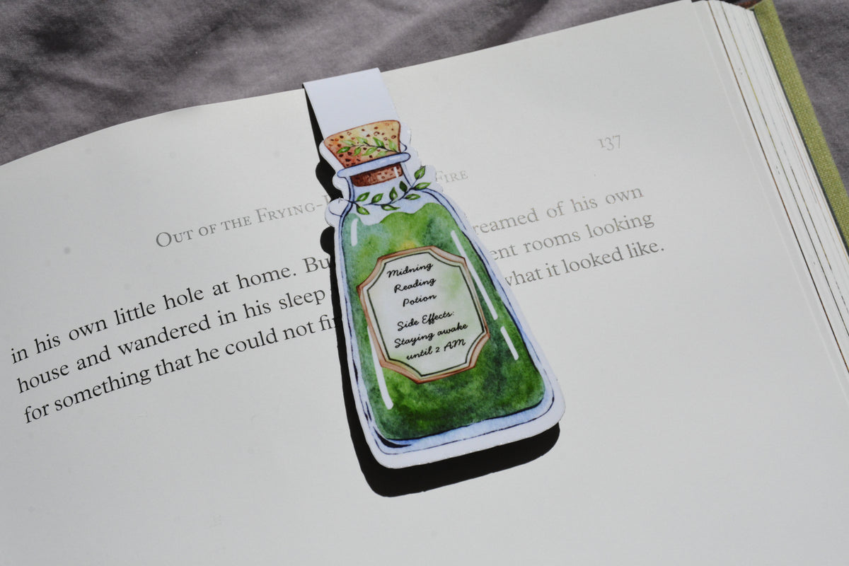 A magnetic bookmark shaped like a green potion bottle with illustrated text, placed on an open book page.