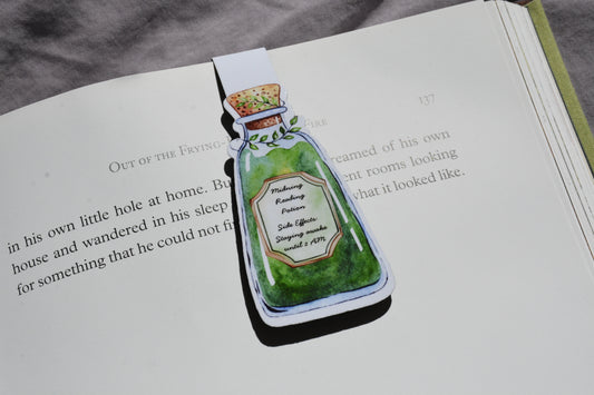 A magnetic bookmark shaped like a green potion bottle with illustrated text, placed on an open book page.