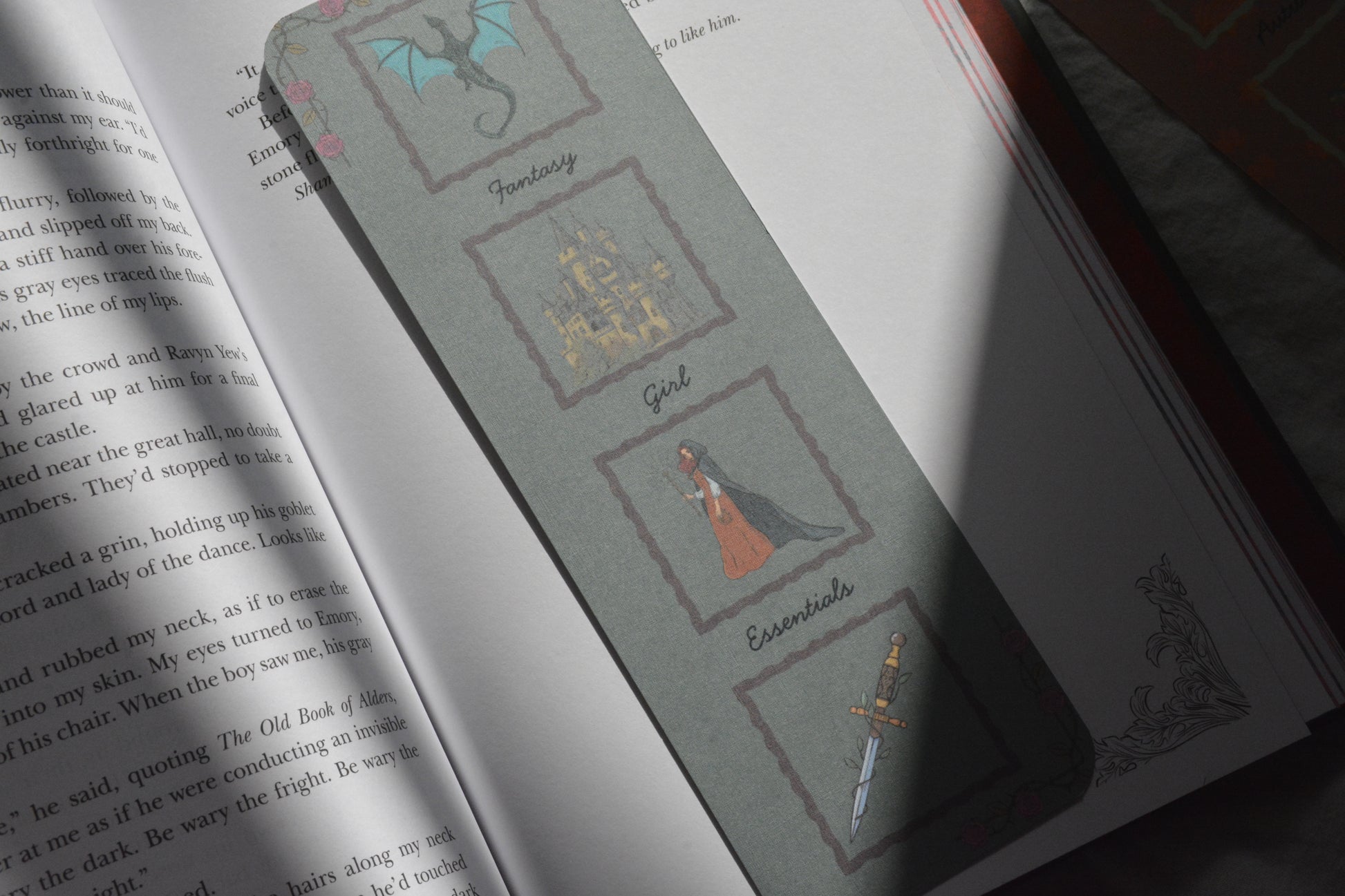 A gray book bookmark with fantasy-themed illustrations, shown resting on an open book.
