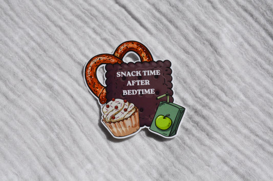 A die-cut sticker featuring a pretzel, a cupcake, and a juice box with the text 'SNACK TIME AFTER BEDTIME' on a white textured fabric background.