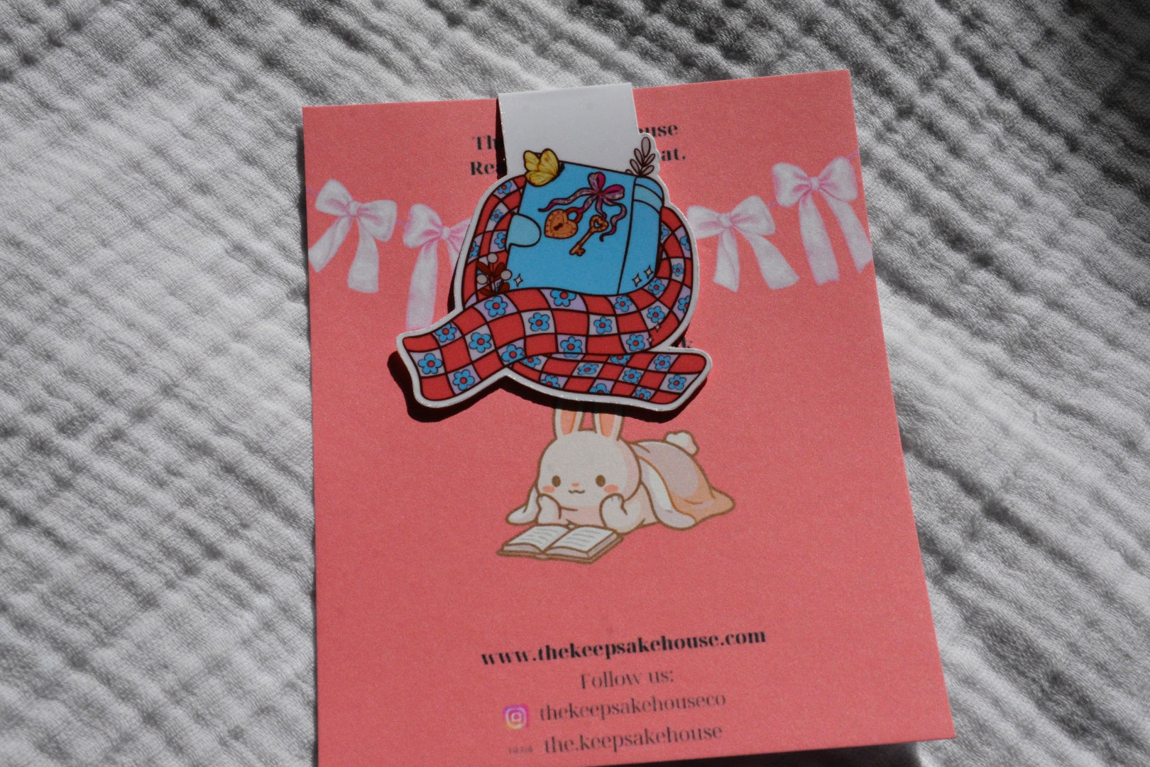 Handmade magnetic bookmark featuring a book wrapped in a cozy scarf design on a pink Keepsake House backing card