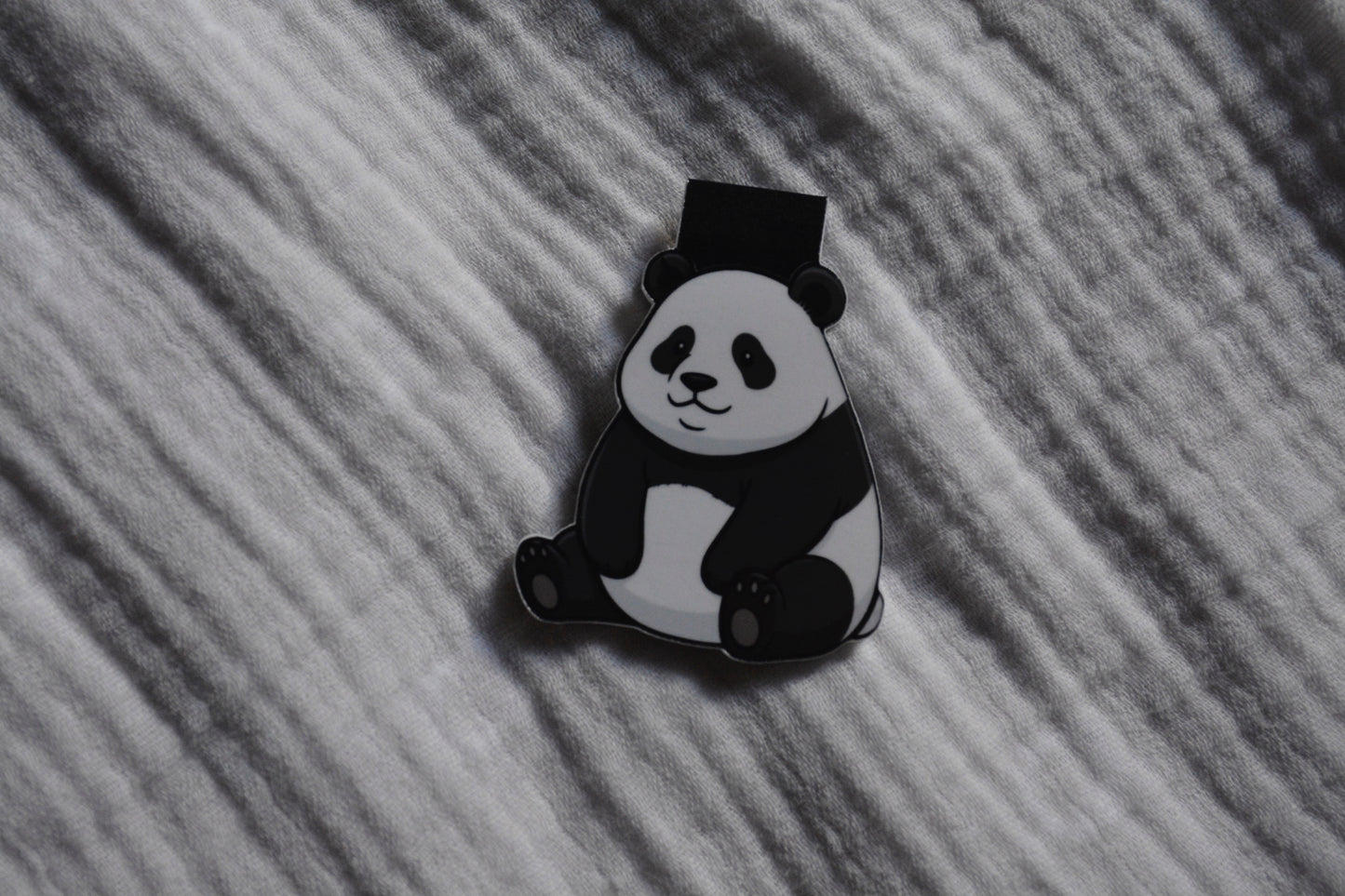 A black and white panda magnetic bookmark placed on a textured gray fabric background.