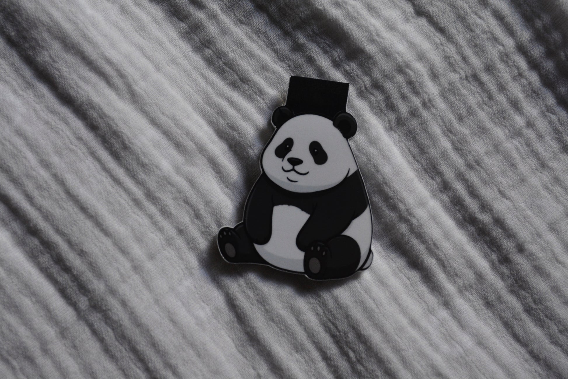 A black and white panda magnetic bookmark placed on a textured gray fabric background.