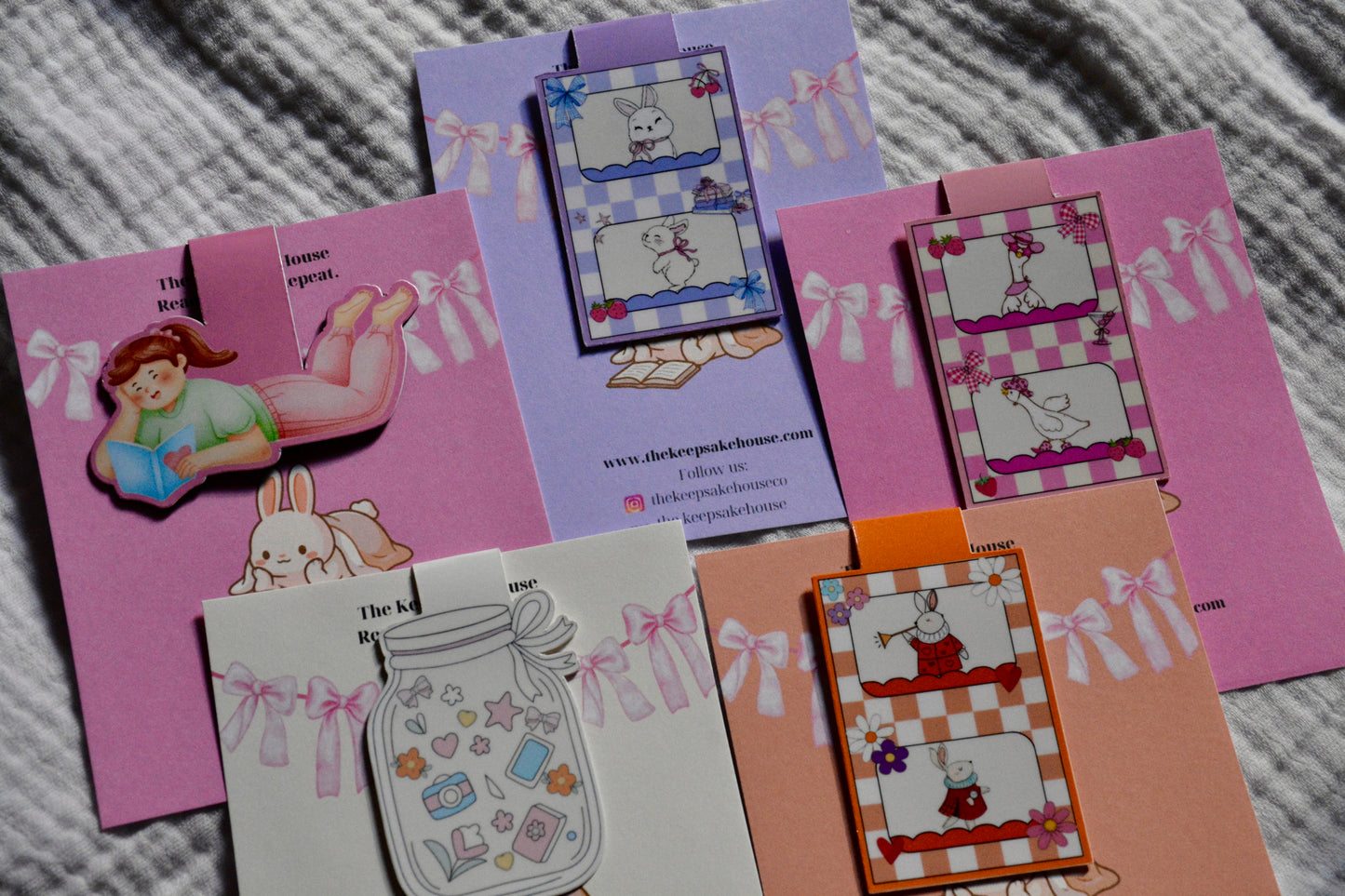 A collection of handmade magnetic bookmarks featuring cute cartoon bunny illustrations, checkered patterns, bows, and whimsical designs, arranged on a gray textured fabric background.