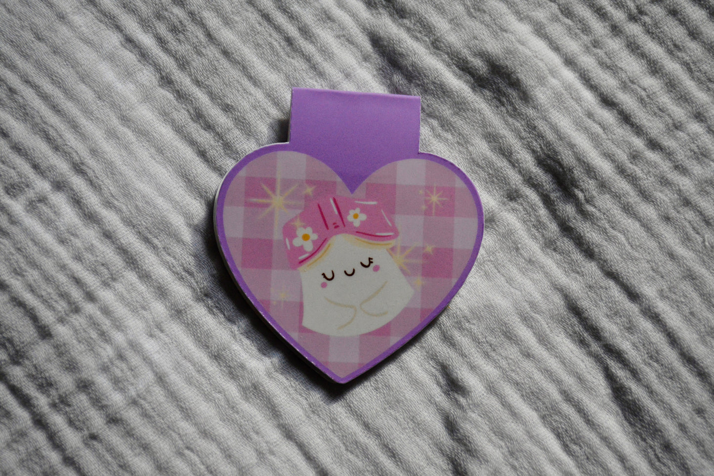 A heart-shaped purple and pink plaid sticker with a cute sleeping cartoon ghost, placed on a gray textured fabric background.