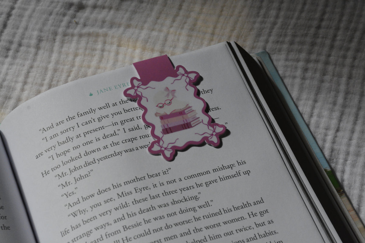 Handmade magnetic bookmark featuring a sleeping ghost with reading glasses on a stack of pink books, displayed on a Keepsake House backing card