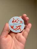 Handmade glitter affirmation sticker featuring watercolor koi fish and the quote "Love surrounds me wherever I go," displayed in hand for Kindles, journals, laptops, and water bottles.