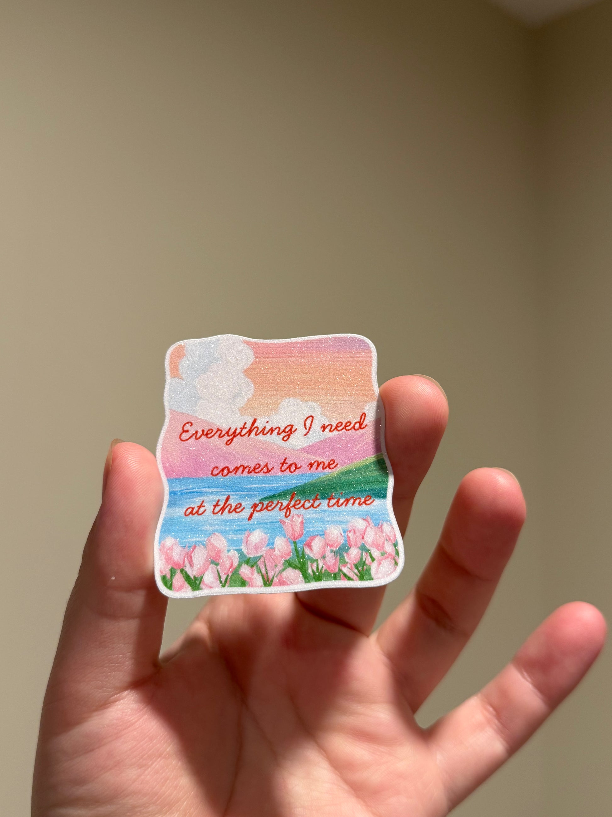 Handmade glitter affirmation sticker featuring a watercolor tulip landscape and the quote "Everything I need comes to me at the perfect time," displayed in hand for Kindles, journals, laptops, and water bottles.