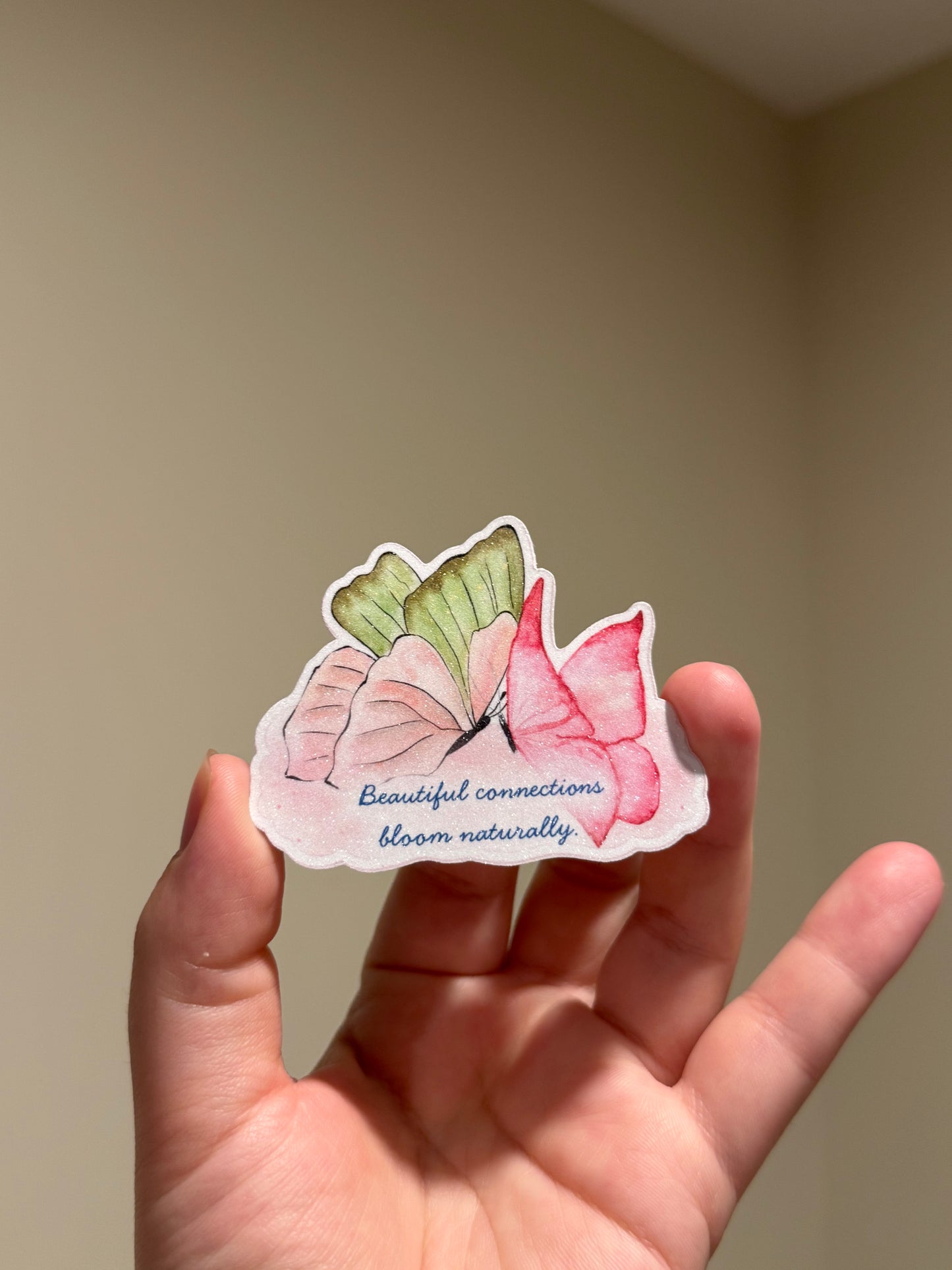 Handmade glitter affirmation sticker featuring watercolor butterflies and the quote "Beautiful connections bloom naturally," displayed in hand for Kindles, journals, laptops, and water bottles.
