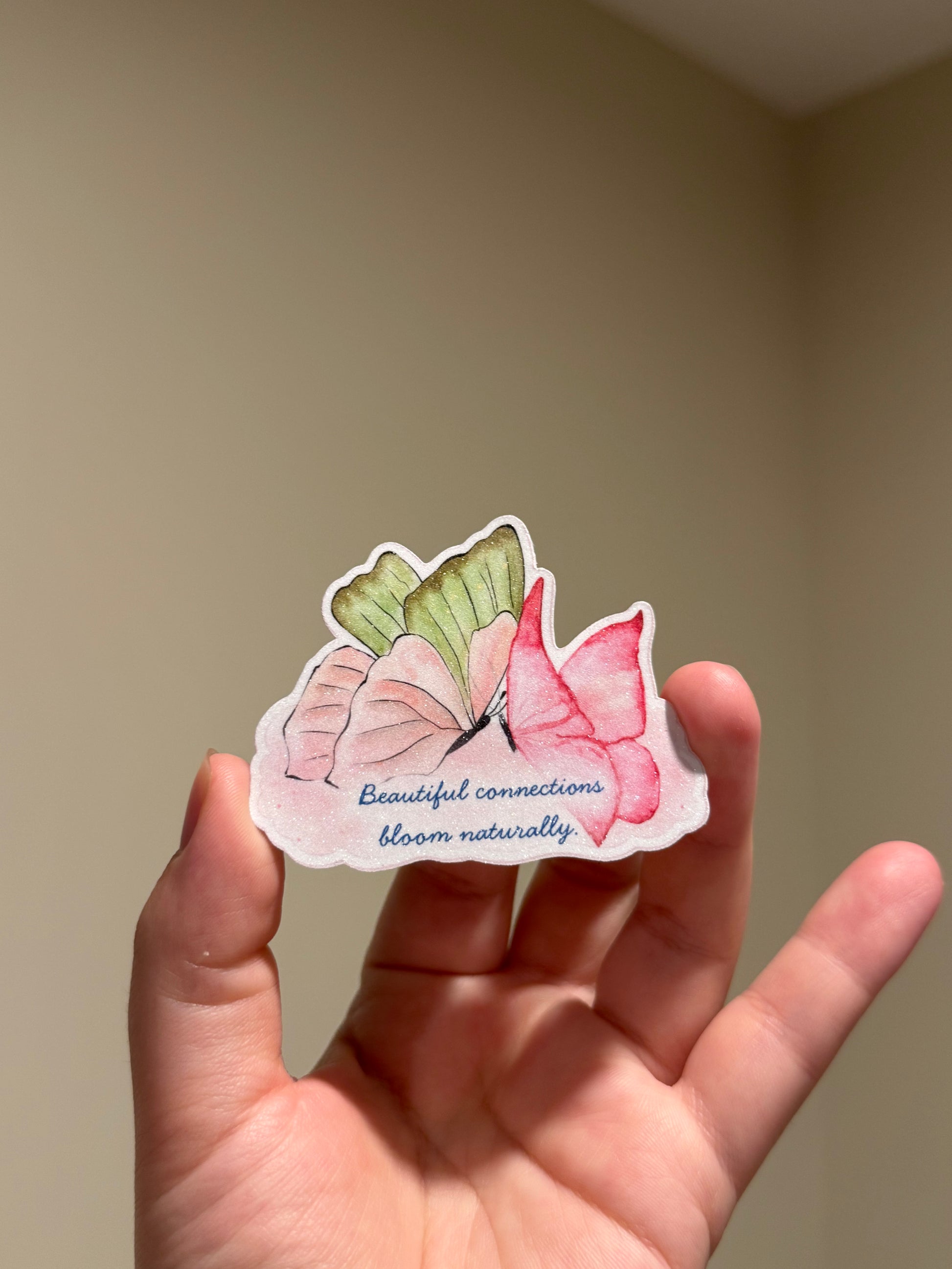 Handmade glitter affirmation sticker featuring watercolor butterflies and the quote "Beautiful connections bloom naturally," displayed in hand for Kindles, journals, laptops, and water bottles.