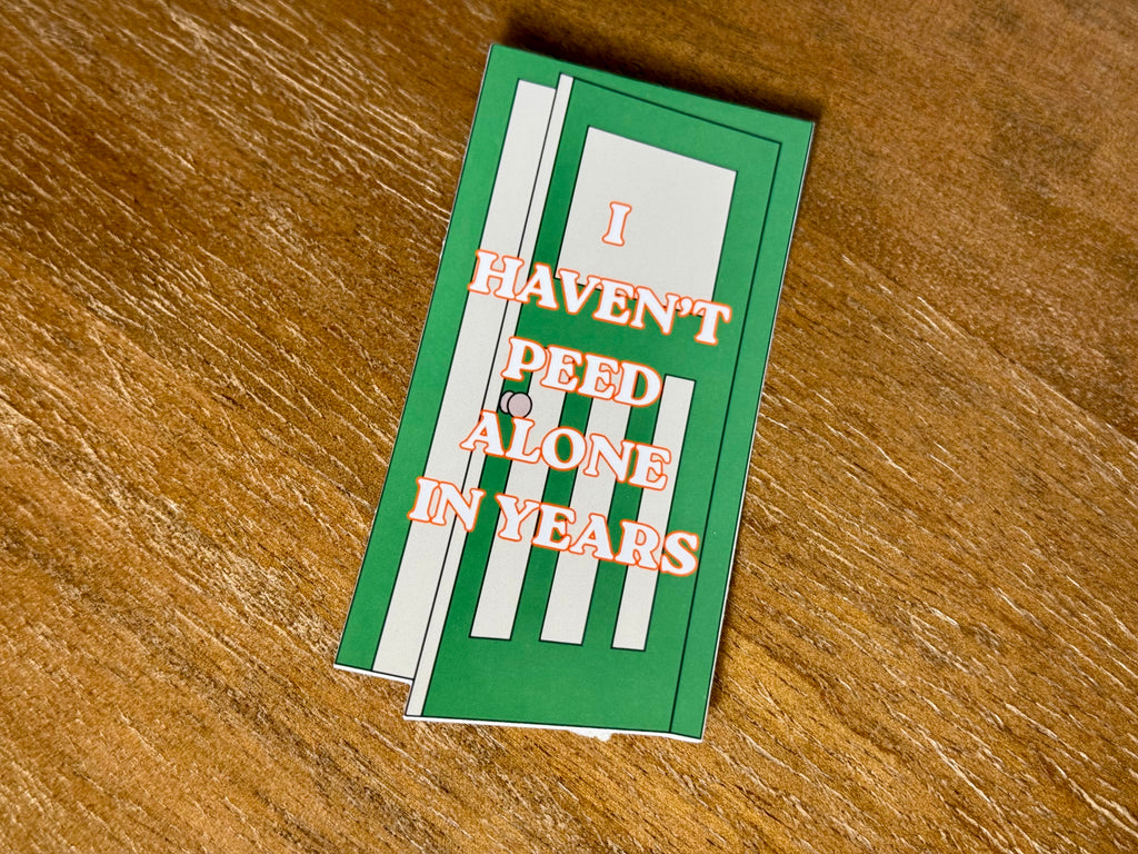 Funny "I Haven't Peed Alone in Years" parenting sticker featuring a green bathroom door design with bold text and a transparent laminate finish.