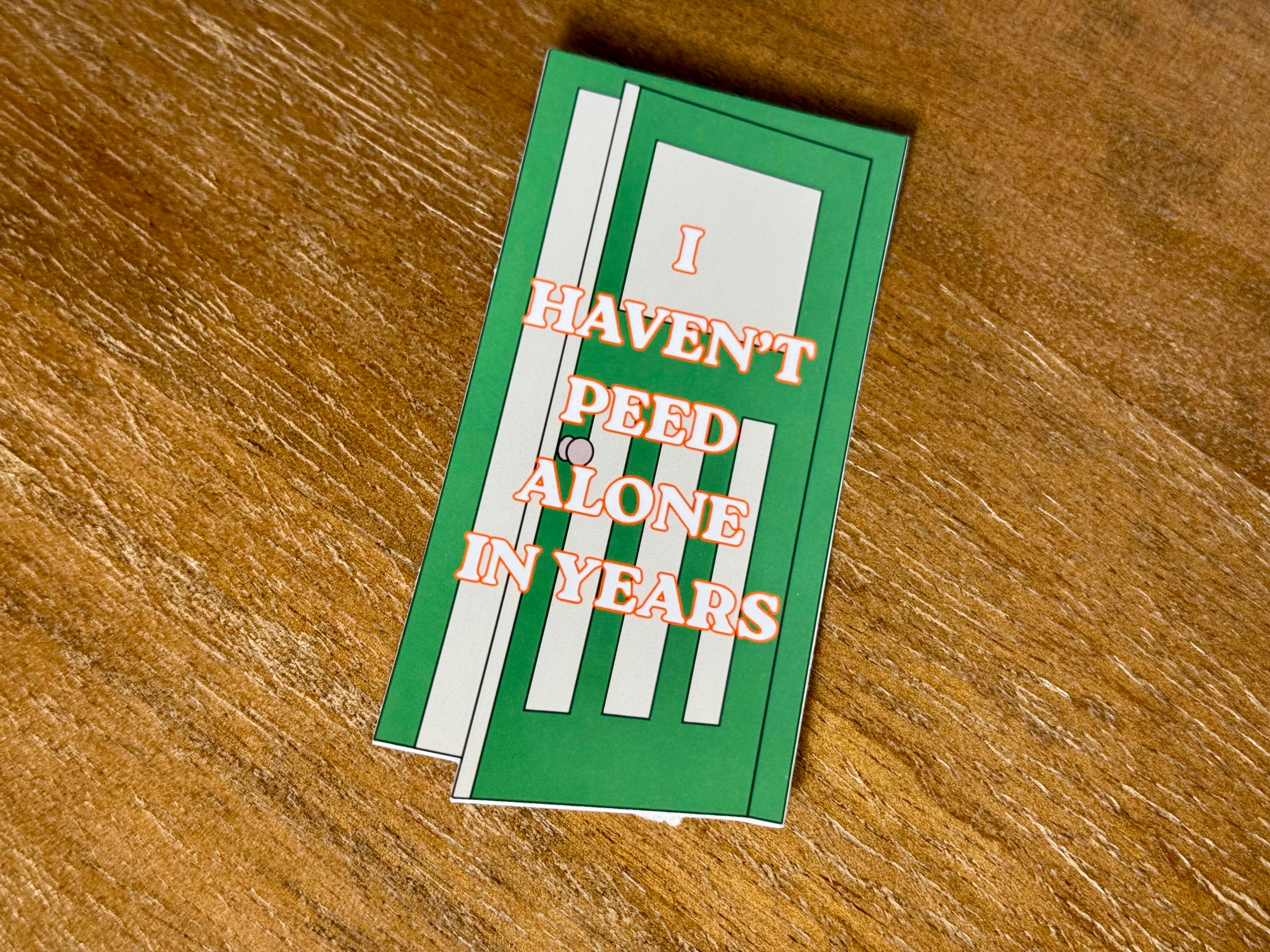 Funny "I Haven't Peed Alone in Years" parenting sticker featuring a green bathroom door design with bold text and a transparent laminate finish.