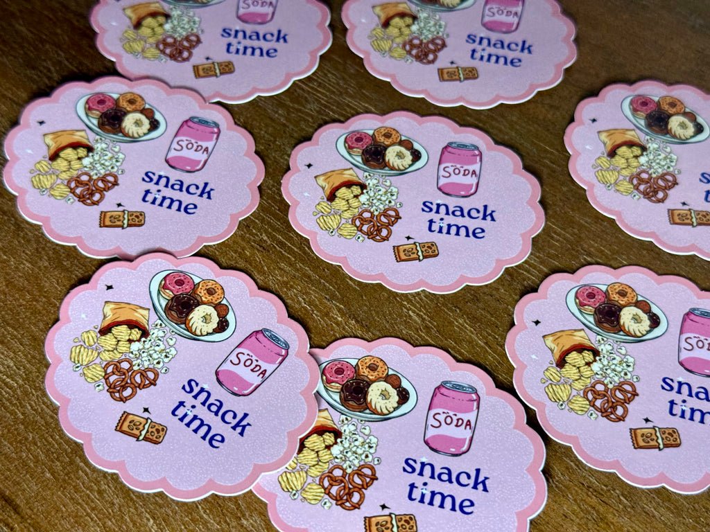 A set of pink scalloped-edged snack time stickers featuring illustrations of donuts, pretzels, chips, and a soda can, arranged on a wooden surface.