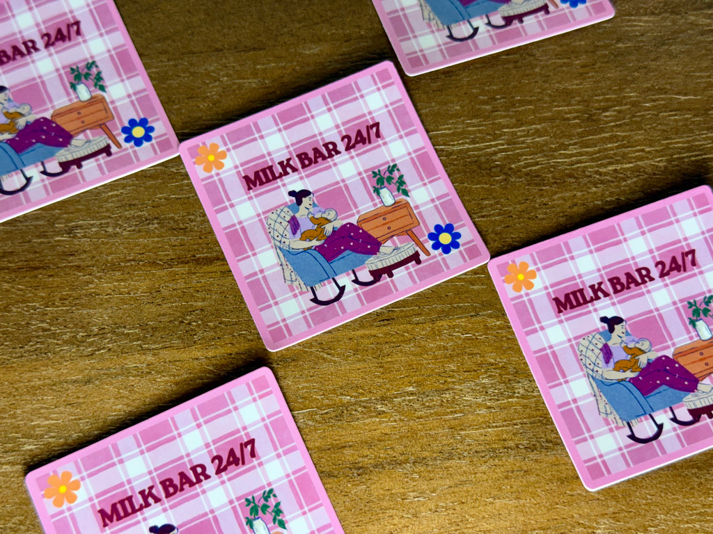 Square coasters with a pink plaid pattern and an illustration of a woman in a rocking chair, with the text 'MILK BAR 24/7' on a wooden tabletop.