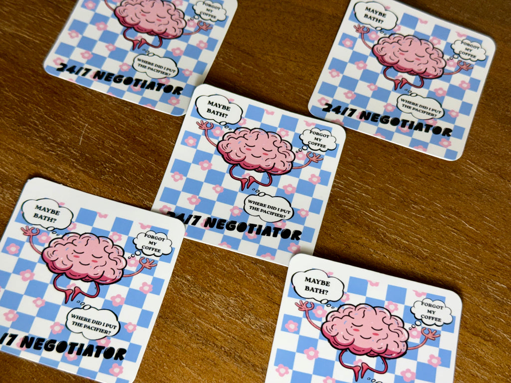 Five square coasters with rounded corners arranged on a wooden tabletop. Each coaster features a pink cartoon brain character with speech bubbles and the text '24/7 NEGOTIATOR' over a blue-and-white check pattern with small pink hearts.