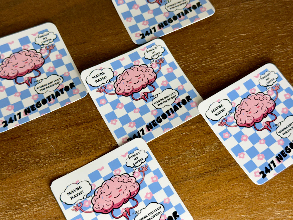 Several square cards with rounded corners arranged on a wooden surface. Each card shows a pink cartoon brain on a blue-and-white checkered background with the text '24/7 NEGOTIATOR' and speech bubbles reading 'MAYBE BATTLE!' and 'I DON'T LIKE WHEN YOU COLD-TASK ME.