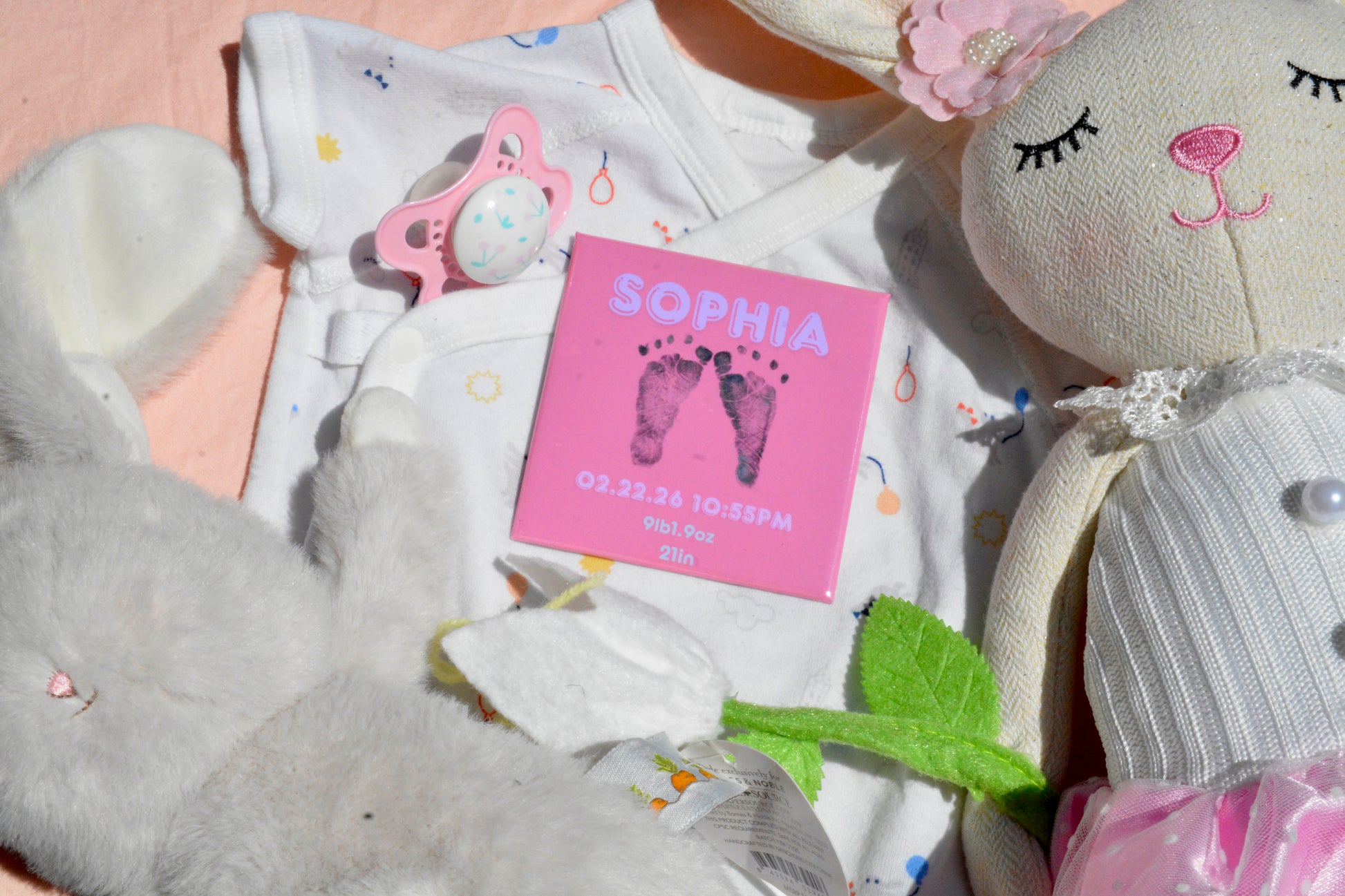 Personalized pink newborn footprint magnet centered on blanket background with birth details.