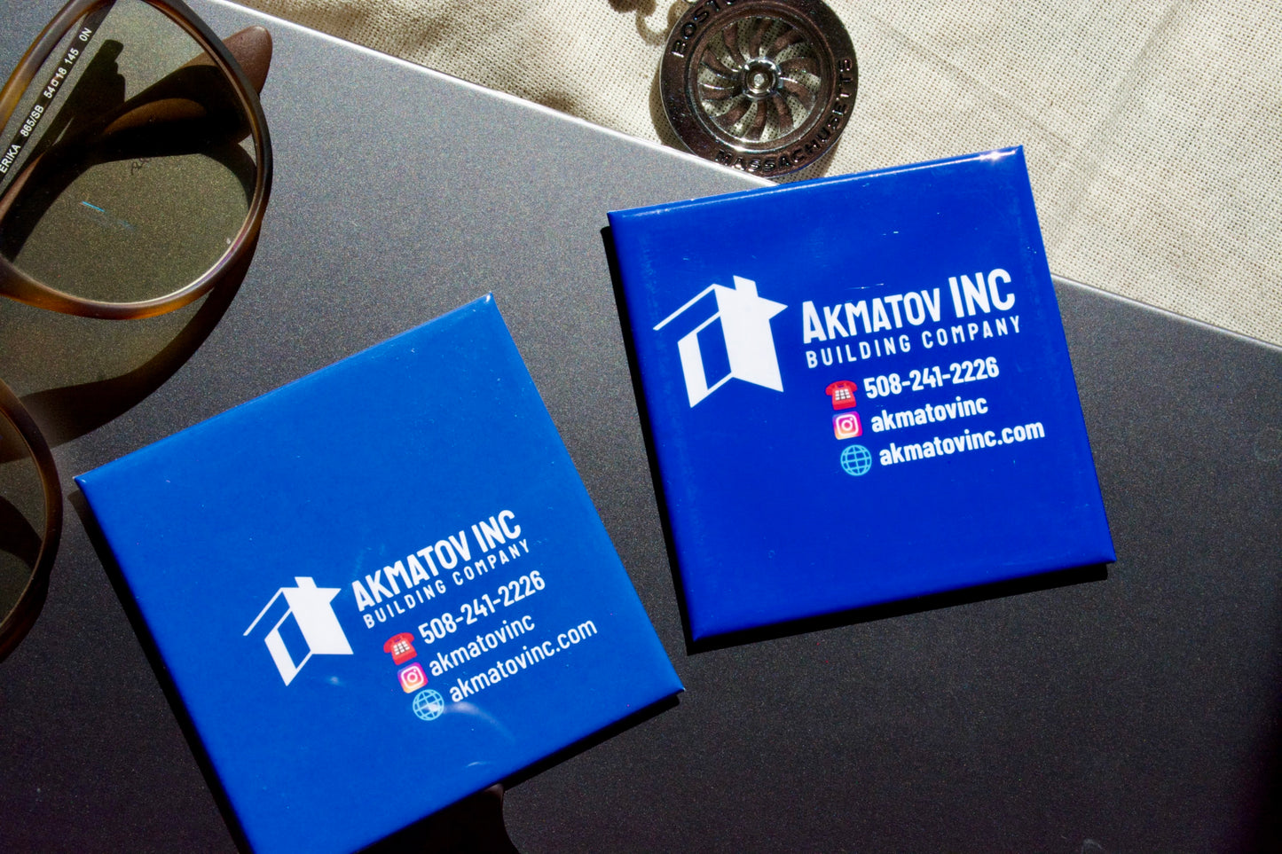 Matte and glossy blue business magnets with business  branding on a dark surface.