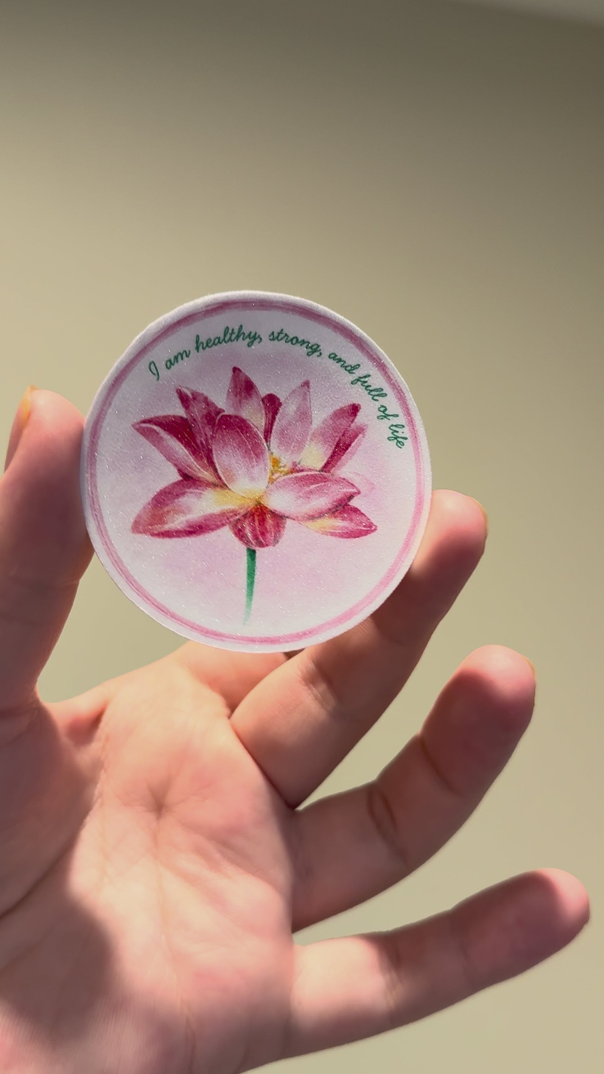 Close-up video showcasing a glitter laminate lotus affirmation sticker with shimmering finish and watercolor floral artwork from multiple angles.
