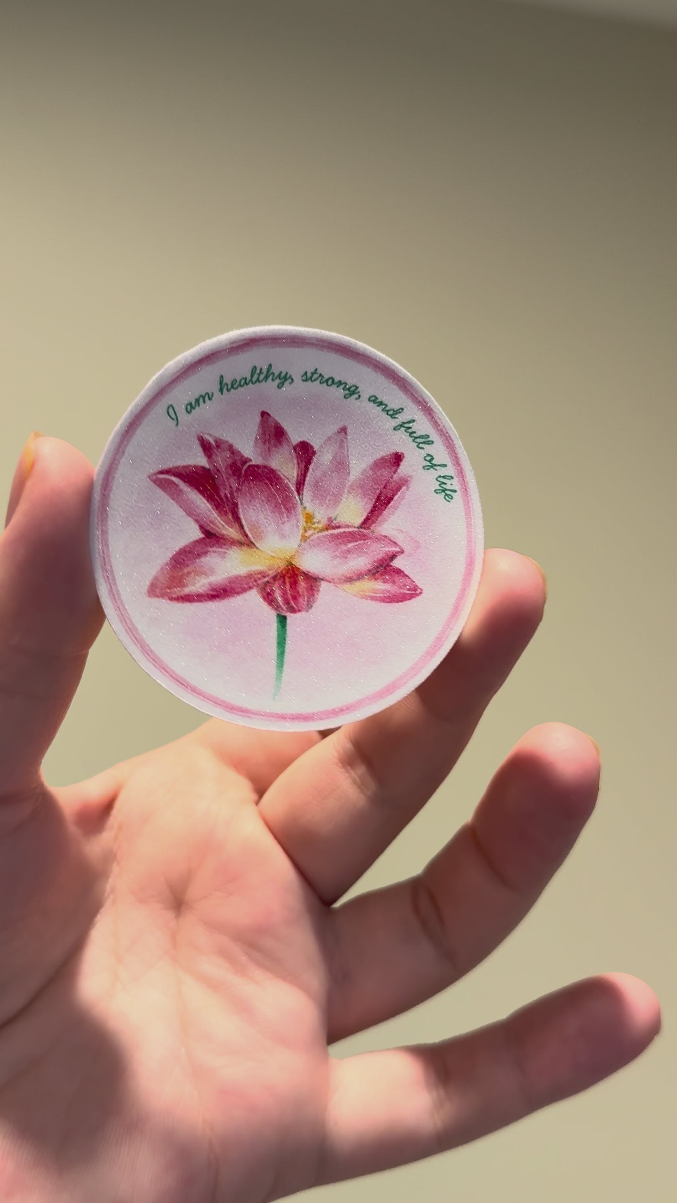 Close-up video showcasing a glitter laminate lotus affirmation sticker with shimmering finish and watercolor floral artwork from multiple angles.