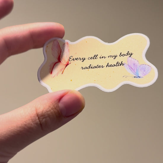 Close-up video of a watercolor butterfly affirmation sticker with glitter laminate, showcasing its shimmering finish, pastel butterfly artwork, and handmade details from multiple angles.