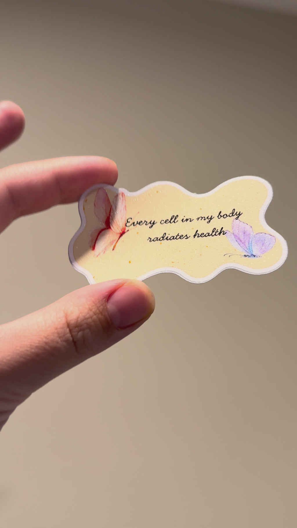 Close-up video of a watercolor butterfly affirmation sticker with glitter laminate, showcasing its shimmering finish, pastel butterfly artwork, and handmade details from multiple angles.