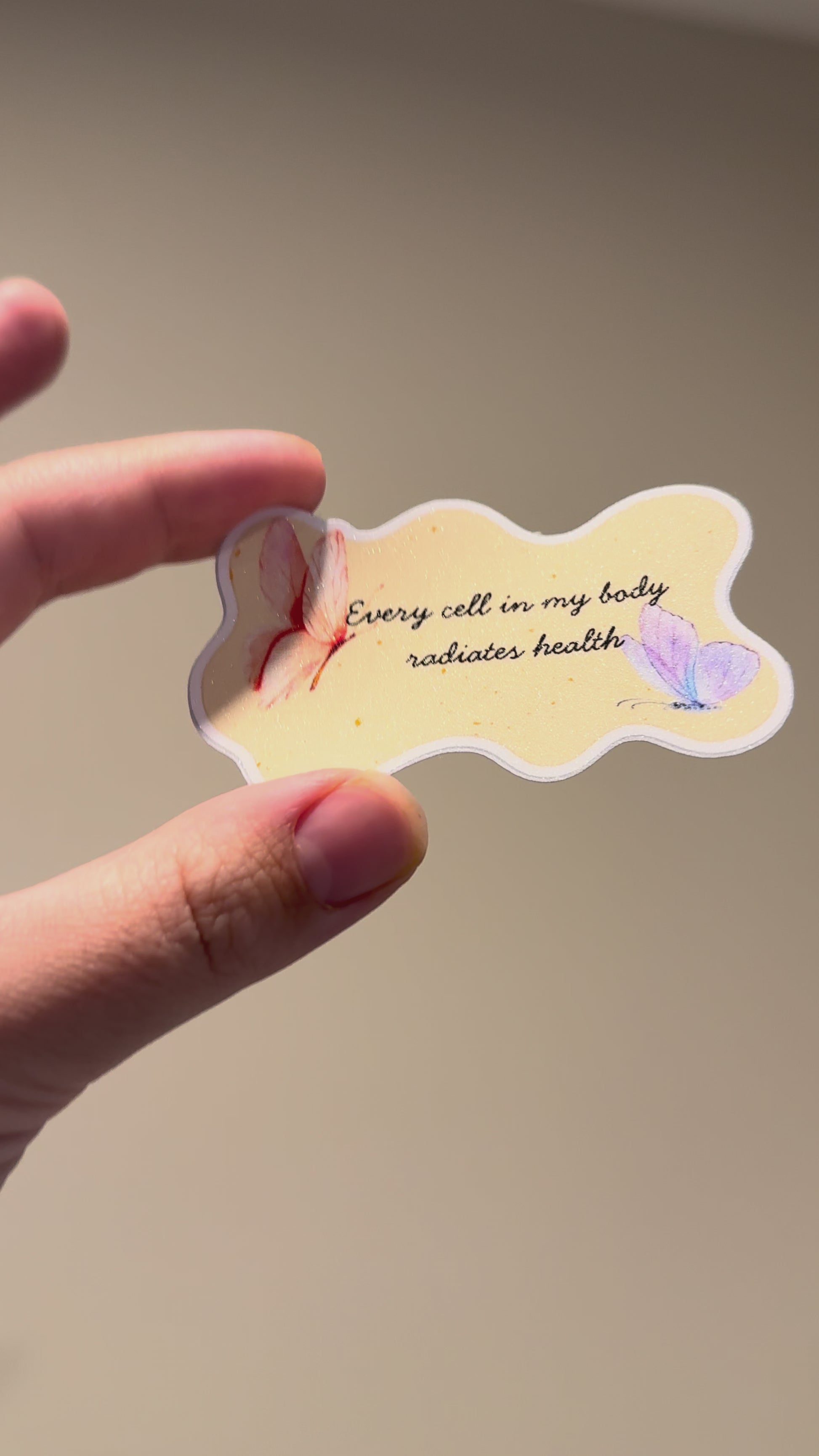 Close-up video of a watercolor butterfly affirmation sticker with glitter laminate, showcasing its shimmering finish, pastel butterfly artwork, and handmade details from multiple angles.